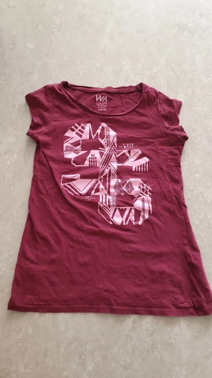 T-shirts - Lila t-shirt från WA Action Sports med coolt grafiskt tryck i ljusrosa på framsidan. Klassisk rund hals och korta ärmar. Tillverkad i mjuk bomull, perfekt för en avslappnad stil. Har ett hål.