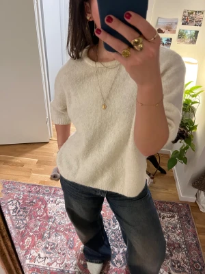 Beige stickad tröja med kort ärm - Säljer en beige stickad tröja med rund hals och korta ärmar. Tröjan har en oversize passform och är gjord i ett mjukt stickat material.