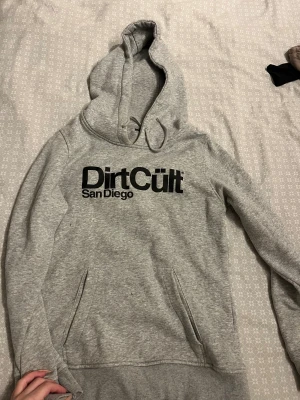 Grå Dirt Cult hoodie  - Snygg grå hoodie från Dirt Cult med svart tryck 'Dirt Cult San Diego' på bröstet. Skön och knappt använd så superfint skick! Inge fläckar eller skavanker, storlek L men sitter som en S då dessa hoodies är väldigt små i storleken☺️