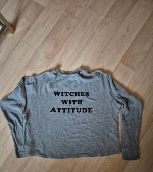 Grå långärmad tröja Pull&Bear - Grå långärmad tröja från Pull&Bear i storlek M med trycket 'WITCHES WITH ATTITUDE' i svart på framsidan. Tröjan har en rund hals och är tillverkad i mjukt, ribbat material som känns skönt mot huden. Perfekt för dig som gillar statement-plagg.