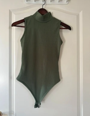 Olivgrön ribbad polobody. Rebecka Stella - Snygg olivgrön polobody i ribbad bomull med ärmlös design. 