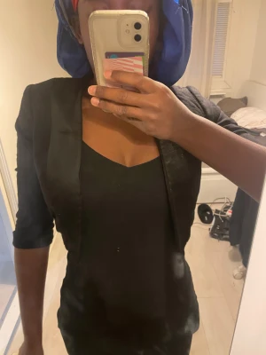 Svart kavaj med trekvartsärm - Snygg svart kavaj med trekvartsärm och klassisk krage. Modellen är kortare och har en slim passform som sitter tajt över axlarna. Materialet är slätt och ger en stilren look, perfekt att styla med en enkel topp eller klänning. Passar xs/xxs