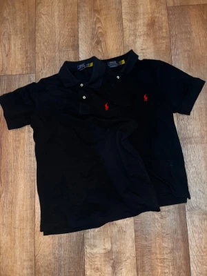 Svart piké från Polo Ralph Lauren - Två svarta pikétröjor från Polo Ralph Lauren med klassisk krage och knappslå framtill. Båda har den ikoniska röda logotypen broderad på bröstet och är i modellen Custom Slim Fit. Perfekt för en clean och stilren look. 100kr/st en i ”M” o en i ”S”