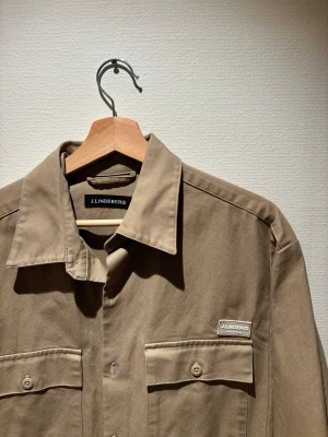 Overshirt - J.lindeberg overshirt i färgen beige, aldrig använd och köptes för 3000:- i deras affär. Den är size medium men skulle säga att den även fits large beroende hur man vill att den ska sitta. Vid några frågor är det bara att höra av er:)