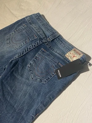 Nya true religon jeans, W29 - Super snygga trendiga true religion jeans i blå med rosa detaljer på sömmen med det ikonsiska märket på fickorna. Helt oanvända med etikett som jag säljer eftersom jag köpte fel storlek🥰