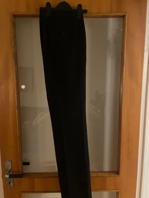 Svarta kostymbyxor Dressmann 32/32 - Använda 3 gånger satt inte så bra på mig bara   Klassiska svarta kostymbyxor från Dressmann i regular fit. Byxorna har raka ben, bälteshällor och knappstängning fram. Materialet är en mix av polyester, ull och elastan som ger en skön känsla och snygg passform. Perfekt för dig som gillar stilrena och tidlösa plagg.         