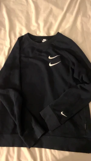 Nike hoodie -Svart med röd text i ryggen - Säljer en unik unisex Nike hoodie som passar både till gymmet och vardags. Storleken är märkt XL, men jag skulle säga att den motsvarar ungefär M den passade mig som vanligtvis har S/M och gav en snygg, lite oversized look. Hoodien är i gott bruksskick. Den har några små fläckar (tandkräm) och tre små prickar från klor längst ner, men det syns knappt. Materialet har hållit sig bra trots regelbunden användning. Perfekt för dig som vill ha en bekväm hoodie med stil