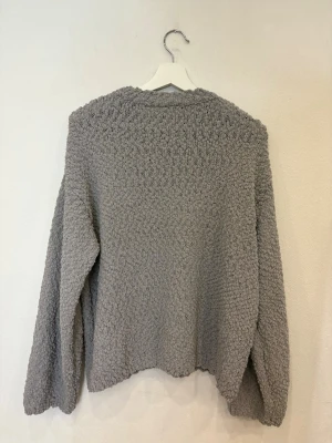 Grå stickad tröja från Divided - Mysig grå stickad tröja från Divided med grov struktur och rund hals. Tröjan har långärmade ärmar och en loose passform som ger en chill vibe. Perfekt för att hålla sig varm under kyliga dagar. Enkel att matcha med jeans eller mjukisbyxor.