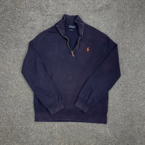 Mörkblå half zip tröja Polo Ralph Lauren - Snygg mörkblå långärmad tröja från Polo Ralph Lauren med orange broderad logga på bröstet. Tröjan har half zip-dragkedja och är gjord i mjuk pima bomull. Perfekt för dig som gillar klassisk stil med en modern touch.