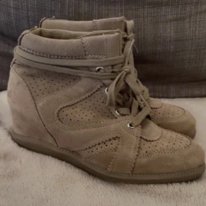 Isabel Marant liknande - Snygga beige sneakers från Pavement med kilklack och perforerade detaljer, jättefina och liknar skorna från isabel marant. Skorna är tillverkade i mjuk mocka och har snörning framtill samt rund tå. Perfekt för dig som gillar en elegant look med lite extra höjd. De är aldrig använda och har kvar prislappen. Nypris är 1699 och jag säljer för 1200kr. Pris går att diskutera, säljer då de är lite för stora.