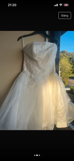 Vit axelbandslös kortklänning med spets - Säljer en vit axelbandslös kortklänning med fluffig tyllkjol och vacker spetsdetalj med pärlor på livet. Klänningen har en romantisk känsla och passar perfekt för student eller bal. Materialet är troligtvis polyester och tyll. Storlek M kan även passa liten L 