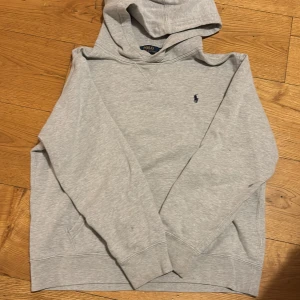 Grå hoodie från Polo Ralph Lauren  - Snygg grå hoodie från Polo Ralph Lauren i storlek XL. Klassisk design med broderad marinblå logga på bröstet, huva och känguruficka. Mjuk bomullsblandning som är perfekt för chill dagar eller när du vill ha en clean look.