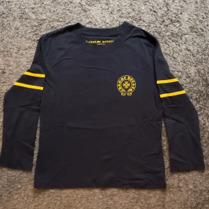 Chrome Hearts svart långärmad tröja - Svart långärmad tröja från Chrome Hearts med gula detaljer. Tryck med logga på bröstet och stort nummer 33 på ryggen. Två gula ränder på varje ärm ger en sportig vibe. Mjuk bomullskvalitet och normal passform. Perfekt för dig som gillar streetwear och snygga prints.