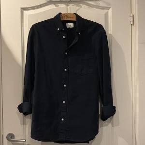 Mörkblå skjorta från H&M - Snygg mörkblå skjorta från H&M med klassisk button-down krage och vita knappar. 