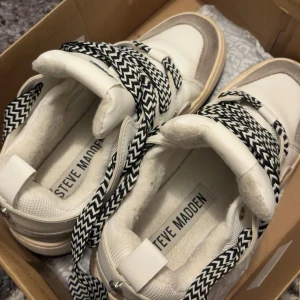 Steve Madden vita sneakers - Snygga vita sneakers från Steve Madden med grå mockadetaljer och tjocka svartvita snören i zigzag-mönster. Dessa är i storlek 39 använda max 4-5 gånger har även sko kartongen kvar 