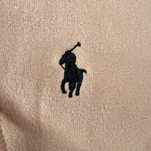 Beige hoodie från Polo Ralph Lauren M - Snygg beige hoodie från Polo Ralph Lauren med klassisk broderad logga på bröstet. Tröjan har huva med snörning, dragkedja framtill och två fickor. Mjuk och skön i bomullsmaterial, perfekt för chill dagar. Passar dig som gillar stilren och enkel look.