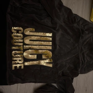 Juicy Couture - Grå velour hoodie från Juicy Couture i storlek S. Jackan har huva, fickor fram och dragkedja. På ryggen finns stora guldiga paljettbokstäver med texten JUICY COUTURE. Perfekt för dig som gillar bling och comfy vibes. Den sitter tajt och skönt, gamla modellen vintage! Svår att hitta