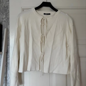 Vit kofta med knytning från Gina Tricot - Supersöt vit  kofta från Gina Tricot med långa ärmar och snygga snörningsdetaljer framtill. Stickad i mjukt material och har rund halsringning. Perfekt att styla med jeans eller kjol för en chill look. Går att knyta om själv 