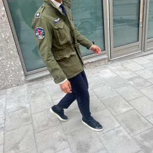  Polo Ralph Lauren Field jacka - Säljer en olivgrön fieldjacka från Polo Ralph Lauren med coola patchar och broderade detaljer på bröstet och ärmen. Jackan har flera stora fickor, snörning i midjan och klassisk krage.