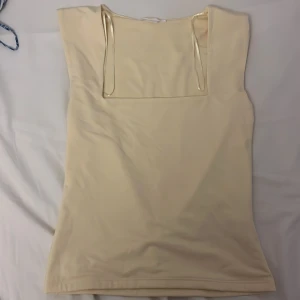 Champagnefärgad klänning Gina Tricot - Smörgul topp från Gina En stilren, ärmlös topp i mjukt och stretchigt material. Den har en modern, rak halsringning och dekorativa tunna band som ger en elegant touch. Perfekt både till vardags och fest  lika fin till jeans som till en kjol. En enkel men chic bas som lyfter hela outfiten.