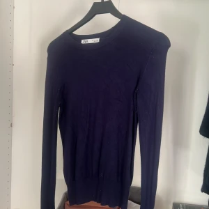 Mörkblå stickad tröja från Zara - Supersnygg mörkblå stickad tröja från Zara med lång ärm och coola guldfärgade knappar vid ärmslutet. Tröjan har rund hals och sitter normalt på kroppen, perfekt för dig som gillar stilrena detaljer och enkel design.