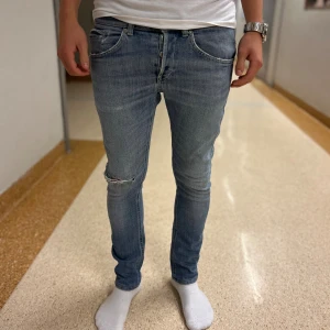 Ljusblå dondup jeans  - Säljer ett par ljusblå dondup jeans med slitning på ena knät. Jeansen har klassisk femficksdesign och smal passform som sitter tajt längs benen. Perfekta för dig som gillar en modern och avslappnad stil.