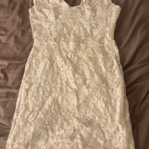 Vit spetsklänning med blommönster - Superfin vit kort studentklänning i spets med blommigt mönster. Klänningen är ärmlös och har en feminin, figurnära passform. Den är oanvänd och är från Missguided 