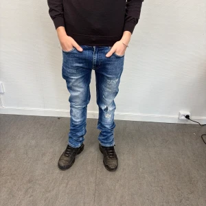 Blå jeans från Emilio Denim Issue - Snygga blå jeans från Emilio Denim Issue med slitna detaljer och en liten reva på ena benet. Modellen har raka ben och klassiska fickor både fram och bak. Jeansen har normal passform och är tillverkade i jeansmaterial med cool tvättad look. Perfekt för dig som vill ha en clean och stilren look!