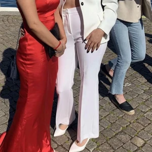 Vita bootcut kostymbyxor från Zara - Snygga vita kostymbyxor från Zara med bootcut passform och hög midja. Byxorna har pressveck framtill och baktill, sidfickor och är tillverkade i ett mjukt, vävt material som ger en clean och fräsch look. 