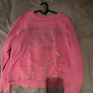 Rosa sweatshirt från Zadig & Voltaire - Cool rosa sweatshirt från Zadig & Voltaire med silverfärgat tryck på bröstet där det står 'Art is truth' och en liten döskalle. Tröjan har rund hals, långa ärmar och mjukt material på insidan. Perfekt för dig som gillar statement-plagg och snygga detaljer.
