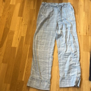 Ljusblå linnebyxor med snörning - Snygga ljusblå linnebyxor med vitt rutmönster och breda uppvikta benslut. Byxorna har elastisk midja med snörning för skön passform och är tillverkade i ett luftigt linnematerial. Perfekta för chill dagar och sommarhäng.