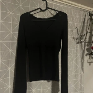 Svart ribbad topp Pernilla Wahlgren - Svart långärmad topp från Pernilla Wahlgren i storlek S. Modellen är ribbad med v-ringad hals och har en slim passform. Materialet är mjukt och stretchigt, perfekt för dig som gillar stilrena och enkla plagg med lite edge.