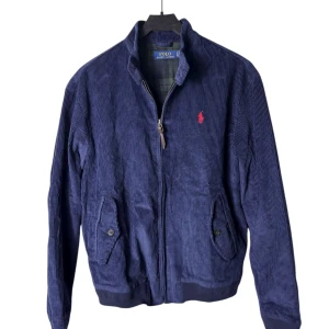 Ralph Lauren Manchester jacka  - Snygg mörkblå bomberjacka från Polo Ralph Lauren i mjuk manchester. Jackan har dragkedja framtill, ribbade muddar och två fickor med knappstängning. Storleken är L i barnstorlek så den passar S