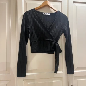 Svart omlottopp från NA-KD - Svart omlottopp från NA-KD med ribbad struktur och långa ärmar. Använd enstaka gånger. Nypris 230kr. Storlek XXS, men passar även XS.