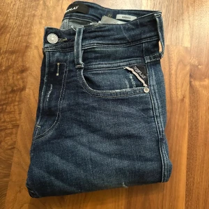Replay Anbass jeans blå straight fit - Snygga Replay Anbass jeans i mörkblå tvätt med slitningar och klassiska fem fickor. Modellen har rak passform och normal midja, med Replay-logga på bakfickan och läderpatch bak. Perfekt för dig som gillar en cool och avslappnad stil.