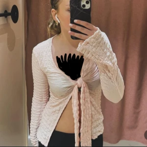 Ljusrosa omlottopp med knyt - Säljer en ljusrosa omlottopp med lång ärm och snygg knytning framtill. Toppen har en ribbad, skrynklig struktur som ger en cool och unik look. Modellen är croppad och har en v-ringad hals. Perfekt för dig som gillar trendiga detaljer och mjuka färger. Från Gina tricot, ny pris runt 300kr. Använd 1 gång men pris går att diskutera 