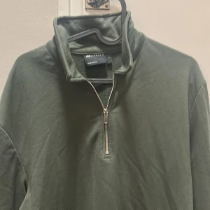 Mörkgrön half zip tröja från asos - Snygg mörkgrön tröja från asos med half zip-dragkedja och hög krage. Perfekt för chill dagar och enkel att matcha med jeans eller joggers. Materialet är mjukt och känns skönt mot huden. Långärmad och loose fit för en avslappnad vibe.