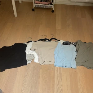 8-pack t-shirts från H&M, Lindex, Esen Sister - Säljer ett paket med 8 t-shirts i olika färger och stilar. Färgerna är svart, vit, beige, ljusblå, grå och en svartvit randig. Alla har rund hals och korta ärmar, vissa är ribbade. Märkena är H&M, Lindex, Esen Sister och 157. Perfekt för dig som vill ha basic och snygga toppar.