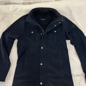 J Lindeberg Jacka - Mörkblå jacka från J lindeberg i strl s. Använd men i väldigt bra skick. Skriv privat för fler frågor/bilder.