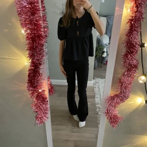 Mörkblå blus med puffärm från 157 - Mörkblå blus från 157 med kort puffärm och knytning vid halsen. Modellen är luftig med rynkad midja och lätt struktur i tyget. Perfekt för dig som gillar en söt och trendig look med volym i ärmarna.