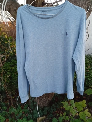Ljusblå långärmad tröja Polo Ralph Lauren - Ljusblå långärmad tröja från Polo Ralph Lauren i mjuk bomull. Klassisk rund hals och diskret mörkblå logga broderad på bröstet. Enkel och stilren design som funkar till jeans eller chinos. Perfekt för dig som gillar clean och avslappnad stil.