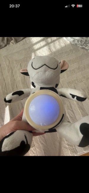 Interaktiv nattlampa ko - Söt interaktiv nattlampa i form av en ko. Lampan lyser med ett mjukt blått sken och är inbyggd i ett mjukt gosedjur. Perfekt för barnrum. Ser ut att vara i mycket fint skick utan synligt slitage eller defekter. Man måste trycka på den och den ändrar färg. När man trycker på den är den igång sen efter ett litet tag måste man trycka ingen