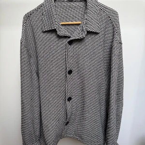 Svartvit rutig skjorta från Zara - Snygg skjorta med svartvitt rutigt mönster och klassisk krage. Skjortan har långa ärmar och svarta knappar framtill. Materialet känns mjukt och har lite struktur, perfekt för dig som gillar en stilren look med lite edge.