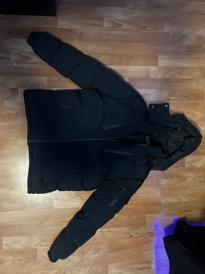 Svart pufferjacka från Brave Soul | S - Svart pufferjacka från Brave Soul med huva och flera praktiska fickor med dragkedja. Jackan har en clean look, långärmade ärmar och är perfekt för kalla dagar. Stängs med dragkedja framtill. Varm och skön säljes då den var för stor för mig. Köpt från Zalando 900 kr 