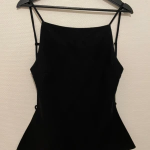 Svart topp med öppen rygg  - Snygg svart topp från Zara med två smala justerbara band på ryggen. Lätt utsvängd nederdel och perfekt för utgång. Lite svårt att se på bilderna så om ni vill kan ni be om bättre. 