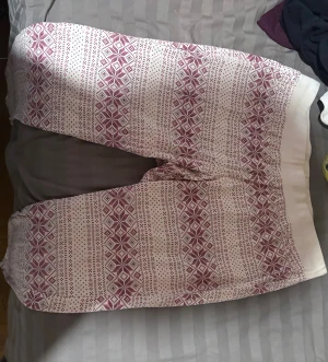 Vita och röda mönstrade mjukisbyxor - Mysiga mjukisbyxor från Cubus i vitt med rött nordiskt mönster. Byxorna har bred resår i midjan och är gjorda i mjuk bomull, perfekta för chill hemma. Passformen är loose och materialet är riktigt skönt mot huden.