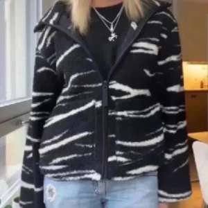 Svartvit teddyjacka med zebramönster - Säljer en svart teddyjacka med vita zebraränder. Jackan har dragkedja framtill, hög krage och är långärmad. Den är fluffig och riktigt skön, perfekt för kyliga dagar. Passformen är normal och materialet känns mjukt och mysigt. BUDA!!!!
