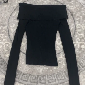 Svart offshoulder ribbad topp - Snygg svart offshoulder topp med långa ärmar och ribbad struktur. Perfekt för dig som gillar en stilren och trendig look. Toppens tighta passform framhäver figuren och den breda kanten upptill ger en cool detalj. Haft på mig bara 2 gånger och priset går o diskuteras 