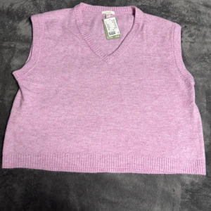 Ljuslila stickad väst från H&M - Superfin ljuslila stickad väst från H&M med v-ringning och ribbade kanter. Perfekt att styla över en skjorta eller t-shirt för en trendig lager-på-lager-look. Västen är mjuk och skön tack vare materialmixen med kashmir och polyester. Helt nya