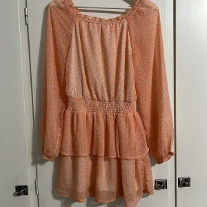 Persikofärgad blommig klänning Kappahl - Supersöt kort klänning från Kappahl i persikofärg med små vita blommor. Klänningen har långa ärmar, smock i midjan och volangdetaljer. Tunt, luftigt tyg med innertyg för extra komfort. Perfekt för vår och sommar!